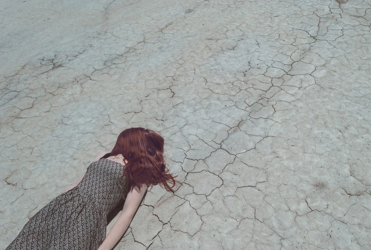 burnout-metaphor-woman-laying-on-cracked-dirt-with-her-hair-covering-her-face